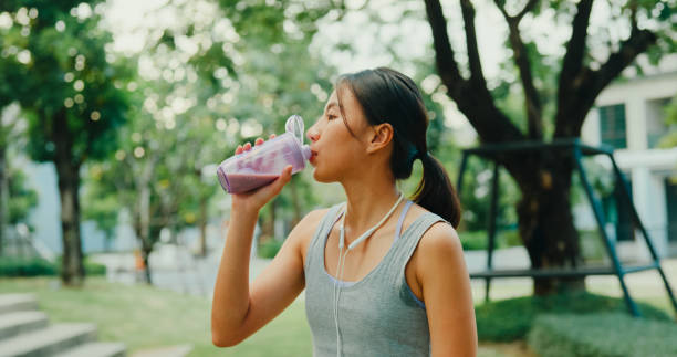 Young Asian female athlete runner drinking protein shake after exercise workout in urban park. Diet and healthy food workout exercise concept.